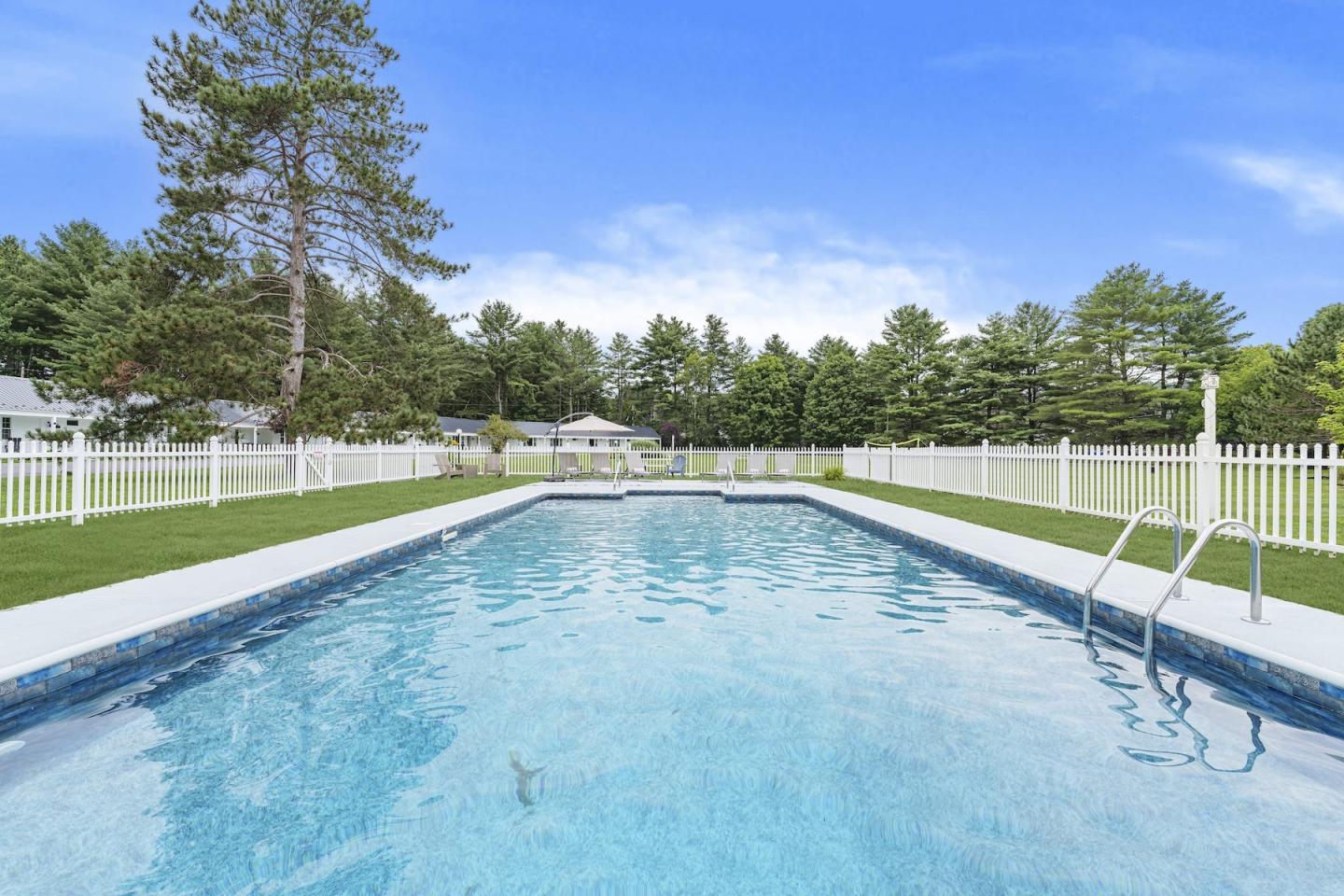 Outdoor swimming pool with clear water, surrounded by trees and a white fence.