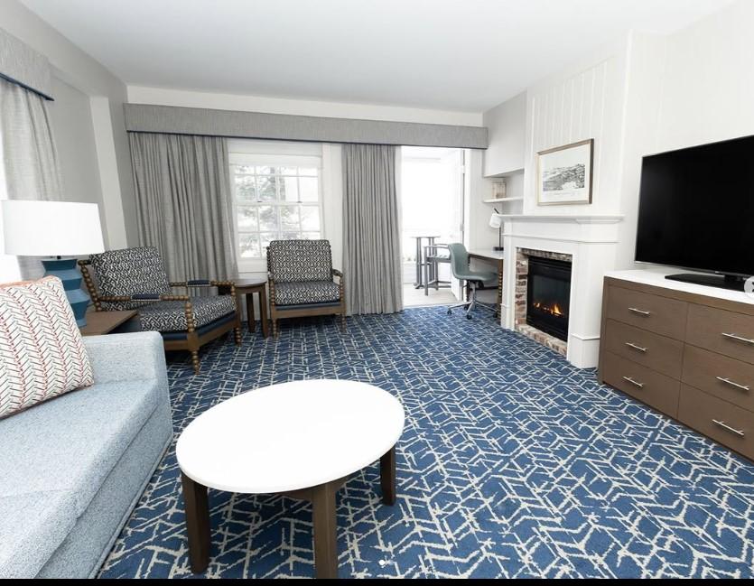 Spacious hotel room with blue carpet, sofa, chairs, fireplace, and TV.