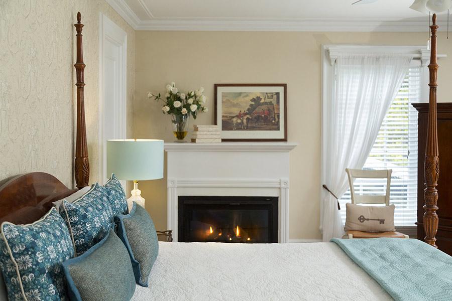 Cozy bedroom with a fireplace, blue pillows, and bright window light.