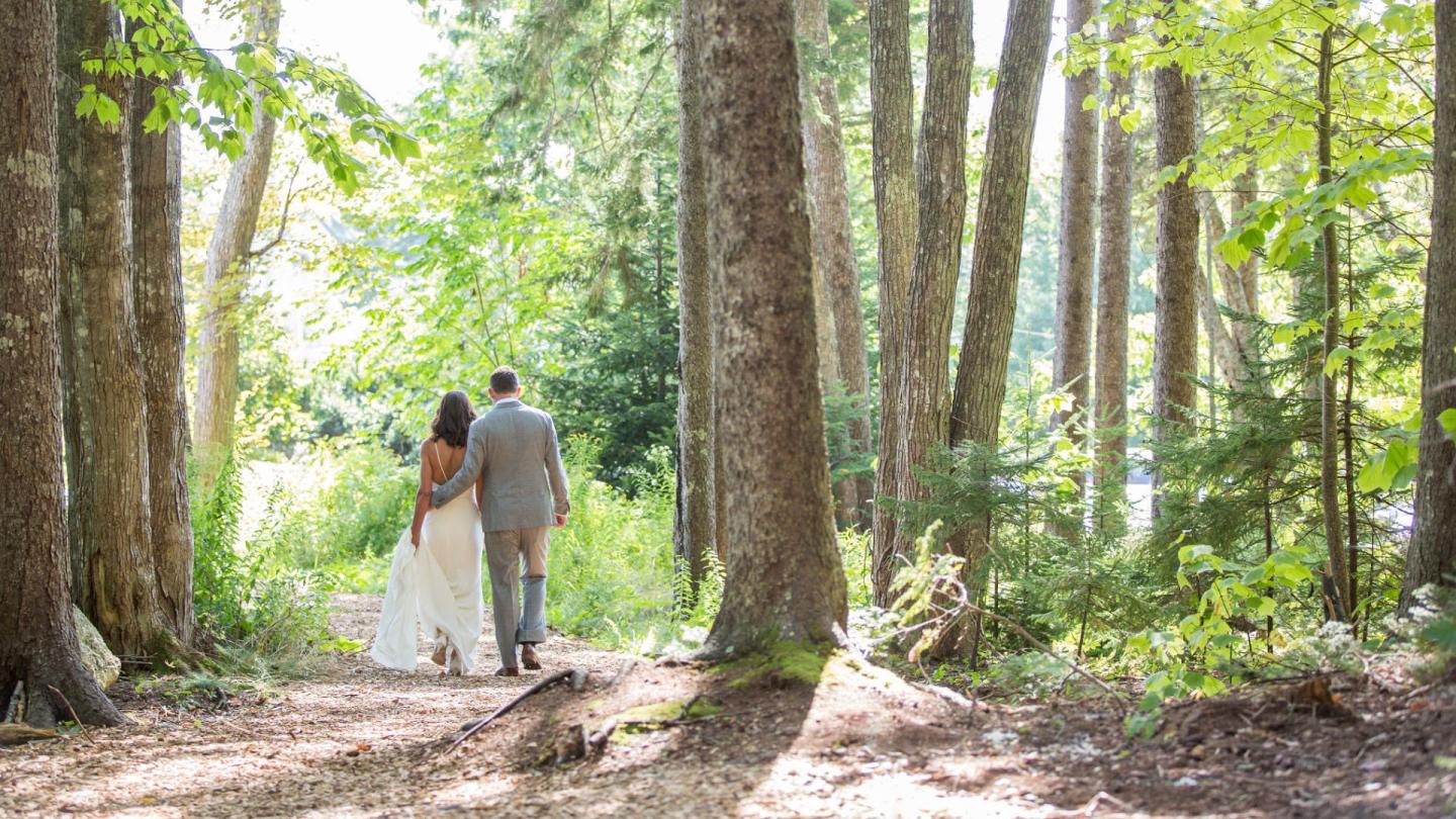 Bride and groom walking in sunlit forest.