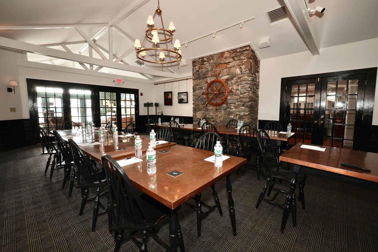 Spacious meeting room with long wooden tables and chairs, a stone wall, and a chandelier.