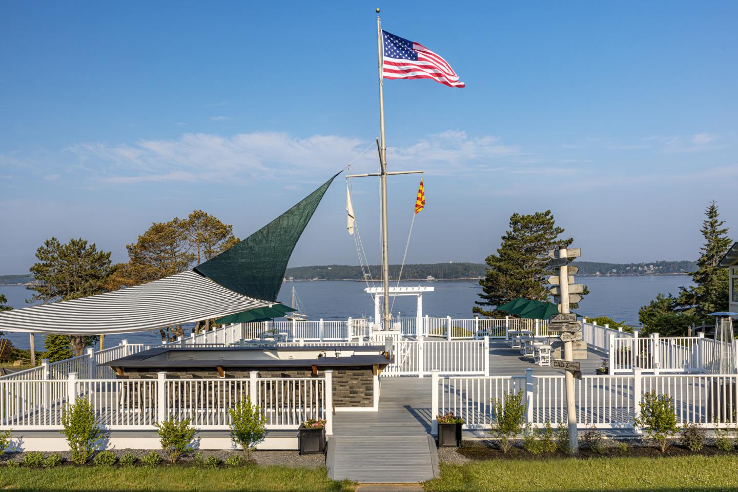 Rooftop deck with flagpoles, overlooking a calm lake under a clear blue sky.