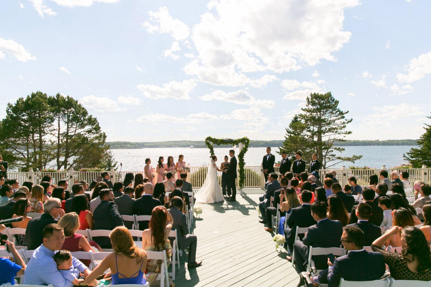 Guests seated at an outdoor wedding ceremony overlooking a lake.