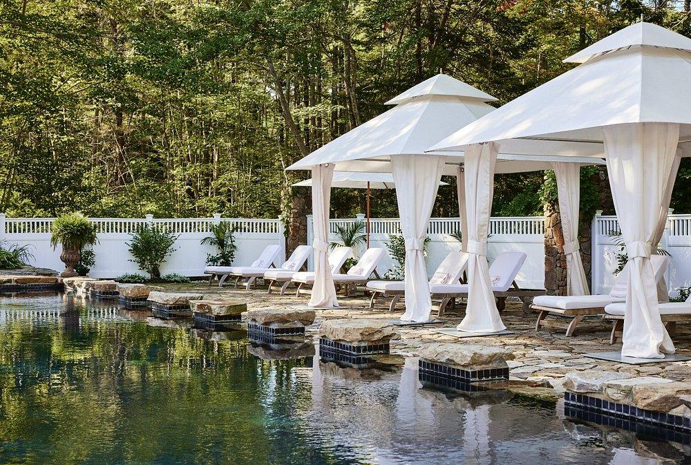 White cabanas by a pool surrounded by trees and lounge chairs.