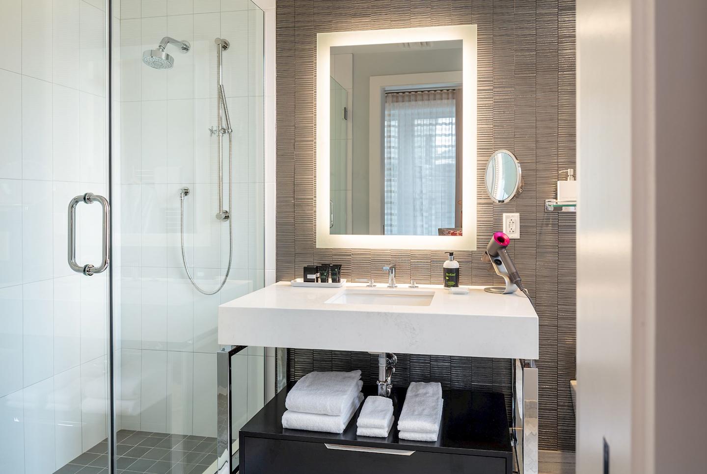 Modern bathroom with glass shower, illuminated mirror, and white sink.