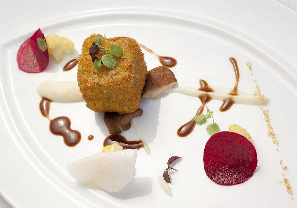 Elegant dish with a crispy cube, sauces, and garnishes on a white plate.