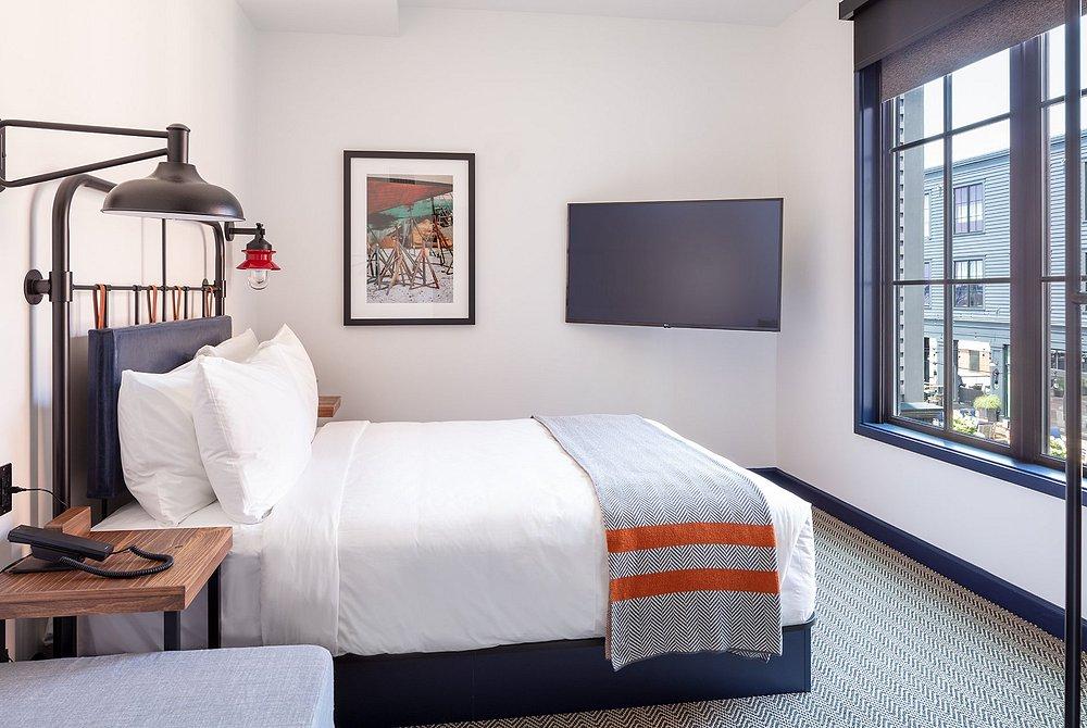 Modern hotel room with a neatly made bed, wall art, and large window.
