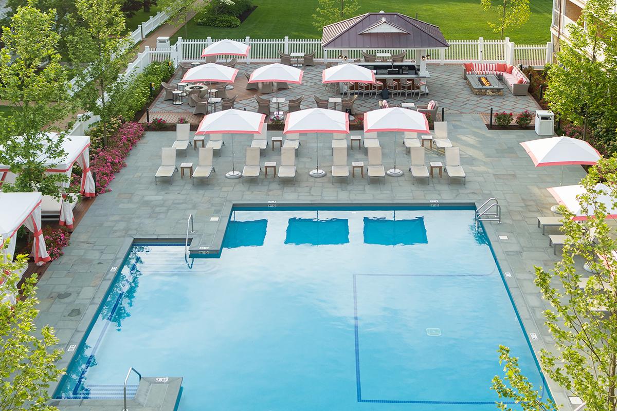 Outdoor pool with loungers, umbrellas, and surrounding greenery.