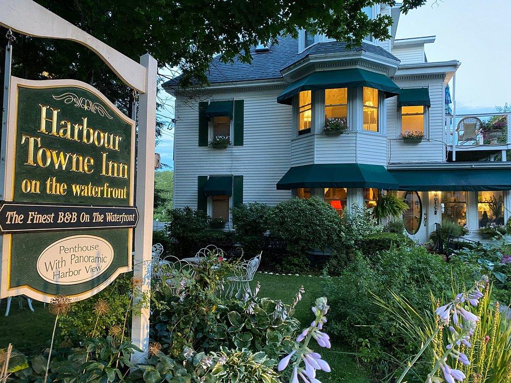 Victorian-style inn with green shutters, surrounded by lush garden at dusk.