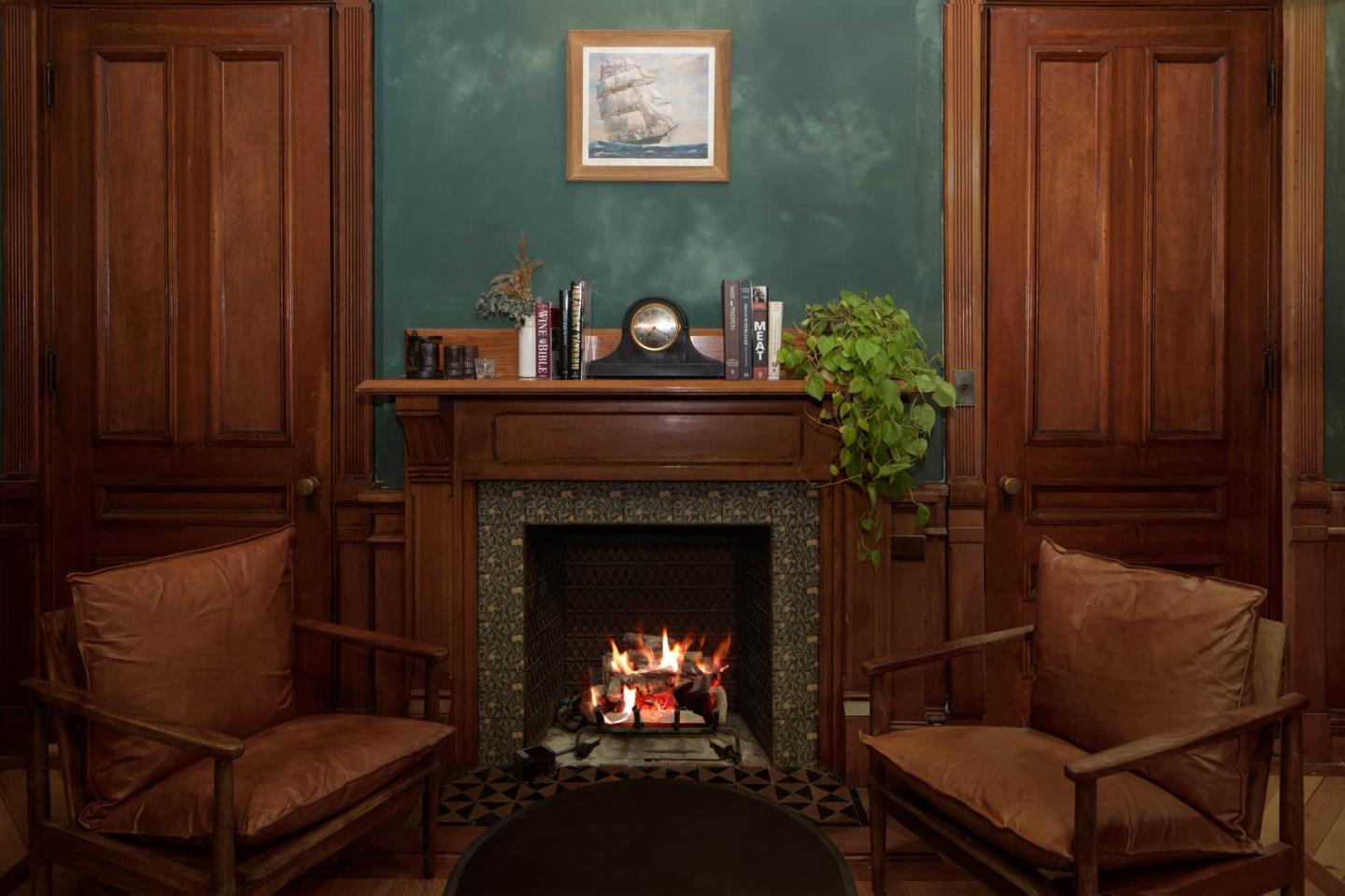 Cozy room with a lit fireplace, brown chairs, and wooden doors.