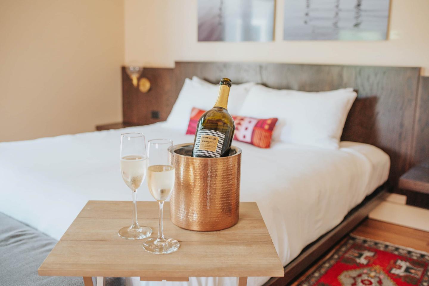 Cozy bedroom with champagne bottle and two glasses on a wooden table.