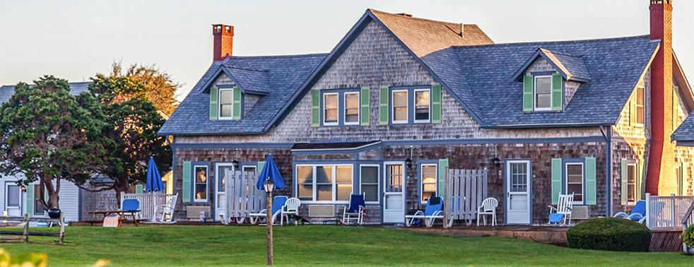 Charming house with blue shutters, lawn, and trees at sunset.