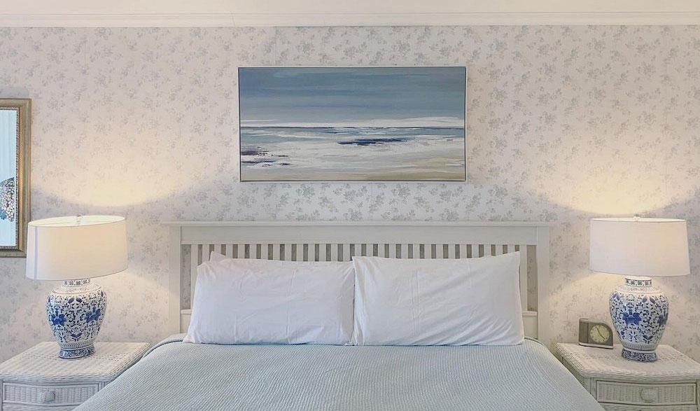 Bedroom with blue bedding, lamps, and seascape painting.