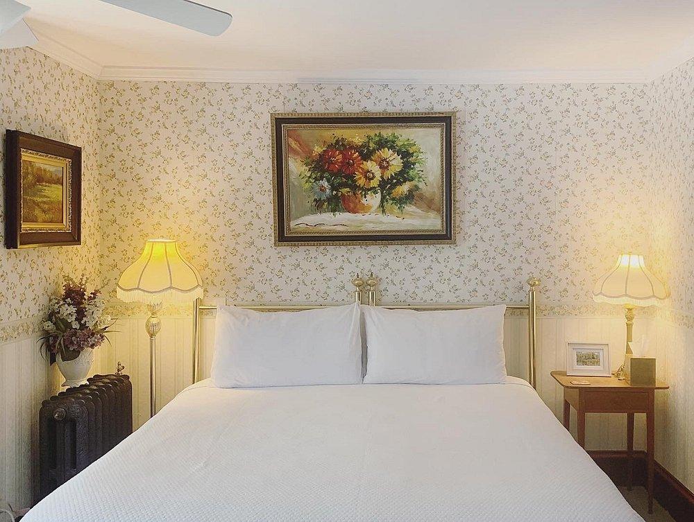 Cozy bedroom with floral wallpaper, framed paintings, and a white bed.