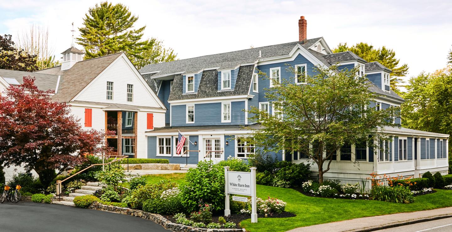 Charming blue and white house with lush garden and American flag.