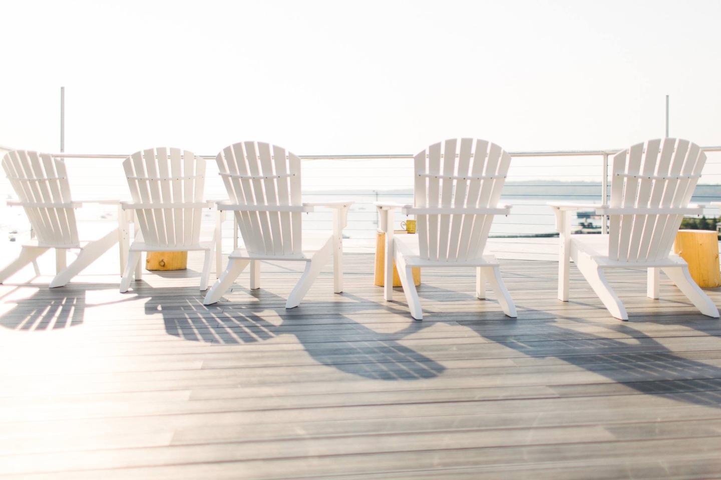 White Adirondack chairs on a sunlit deck, overlooking the sea.