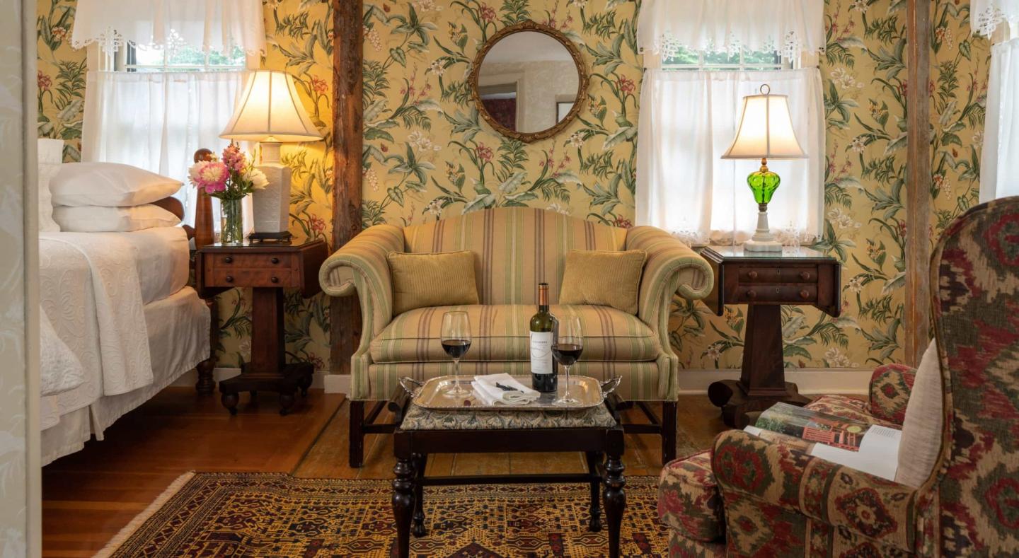 Cozy room with a floral patterned sofa, armchairs, lamps, and a wine bottle on the table.
