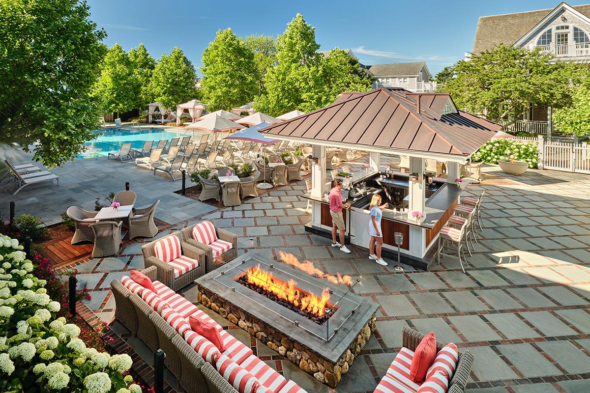 Outdoor patio with fire pit, bar, striped seating, and pool nearby.