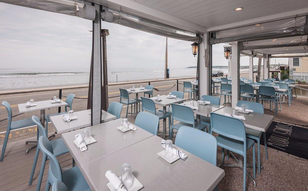 Outdoor seaside restaurant with blue chairs and empty tables.