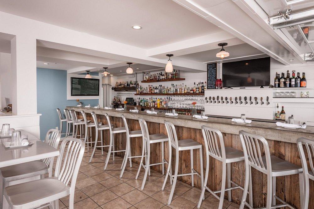 Bar with wooden stools, bottles on shelves, and taps behind the counter.