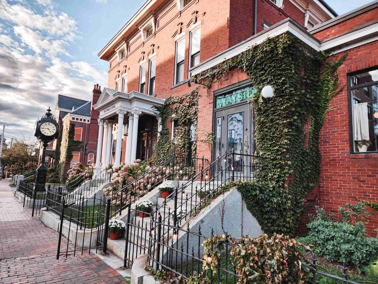 Red brick building with ivy, white pillars, and a street clock.