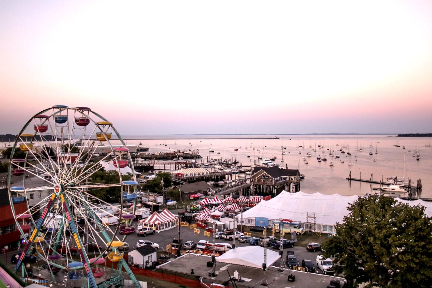 Carnival with ferris wheel at sunset by a waterfront.