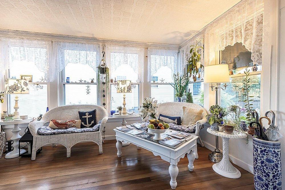 Bright sunroom with white wicker furniture, wood floor, and nautical decor.