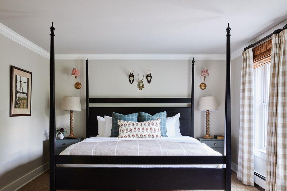 Four-poster bed in a cozy bedroom with lamps and plaid curtains.