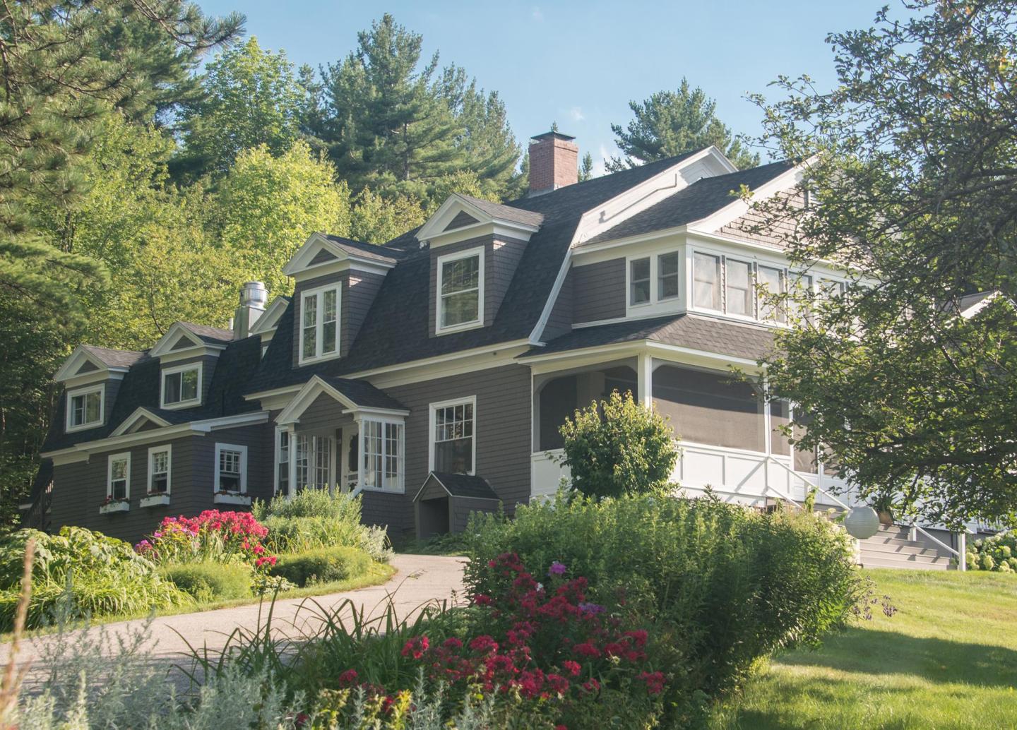Large house with a steep roof, surrounded by gardens and trees, under a clear blue sky.