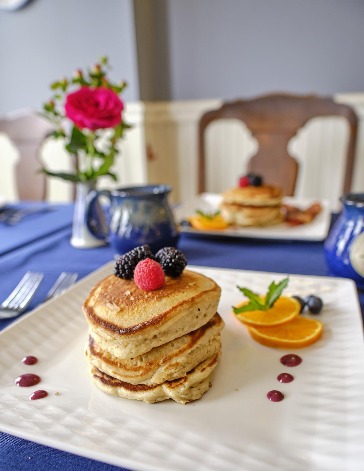 Stack of pancakes with berries and orange slices.