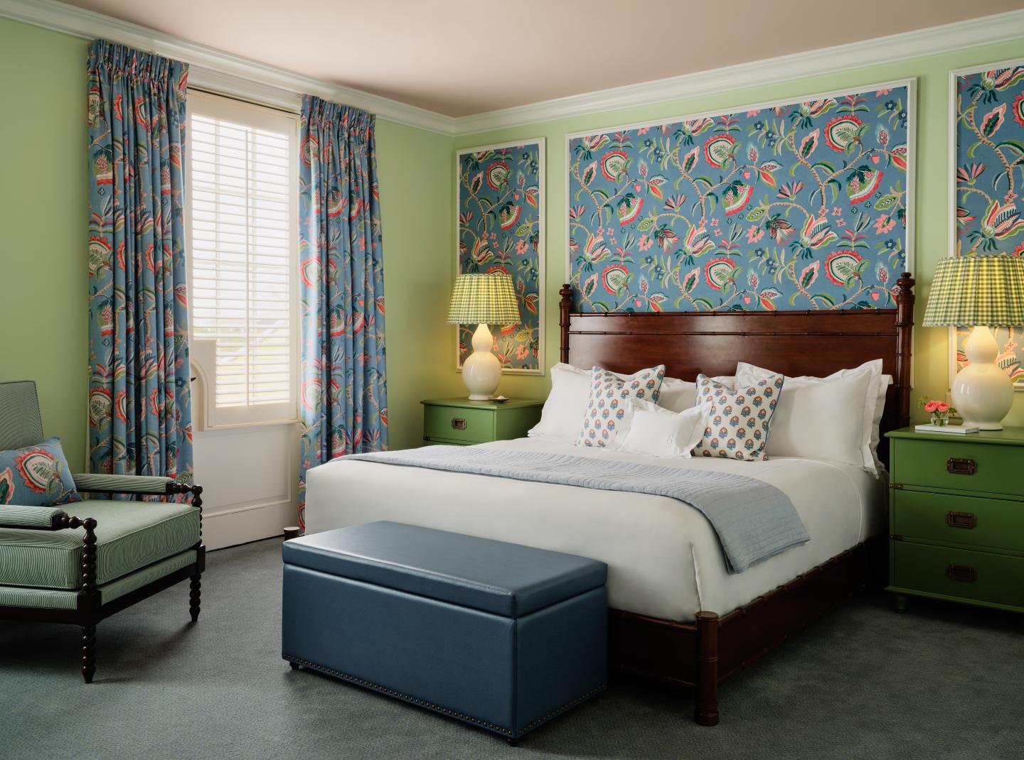 Cozy bedroom with floral wallpaper, green walls, armchair, and a wood-framed bed.