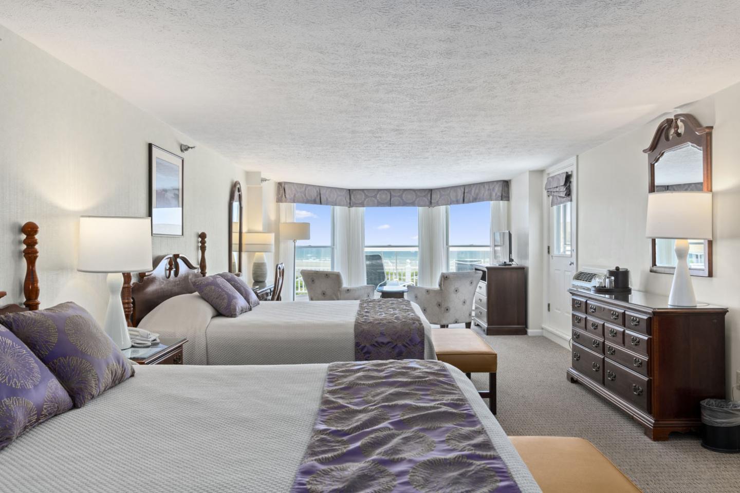 Bright hotel room with two beds, ocean view, and modern decor.