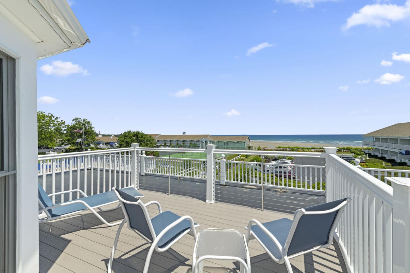 Sunny deck with patio chairs overlooking a calm ocean and clear blue sky.