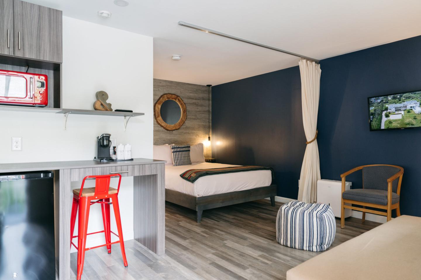 Modern hotel room with bed, red chair, and TV; blue accent wall.