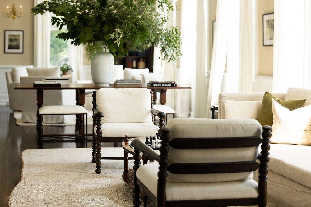 Bright living room with white furniture, large plants, and soft natural light.
