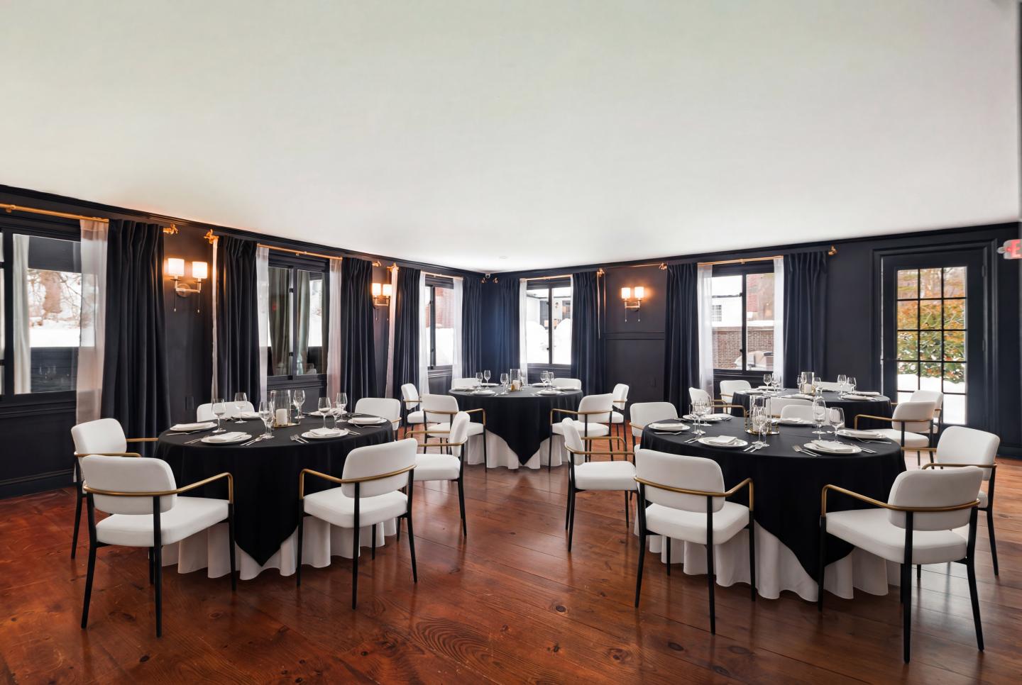 Elegant event room with round tables, white chairs, and black tablecloths.