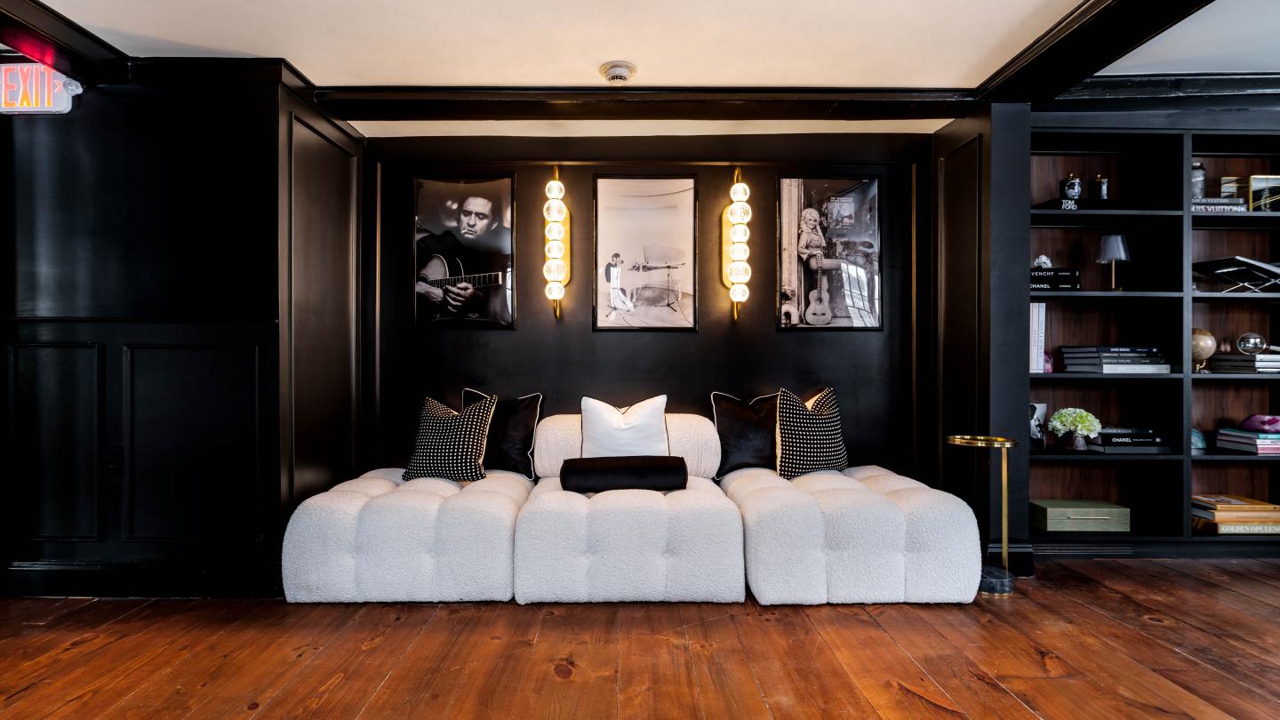 White sofa with pillows against dark wall, framed photos above, wooden floor.