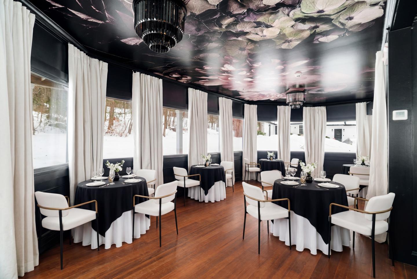 Elegant dining room with black tablecloths and white chairs, wooden floor, floral ceiling.
