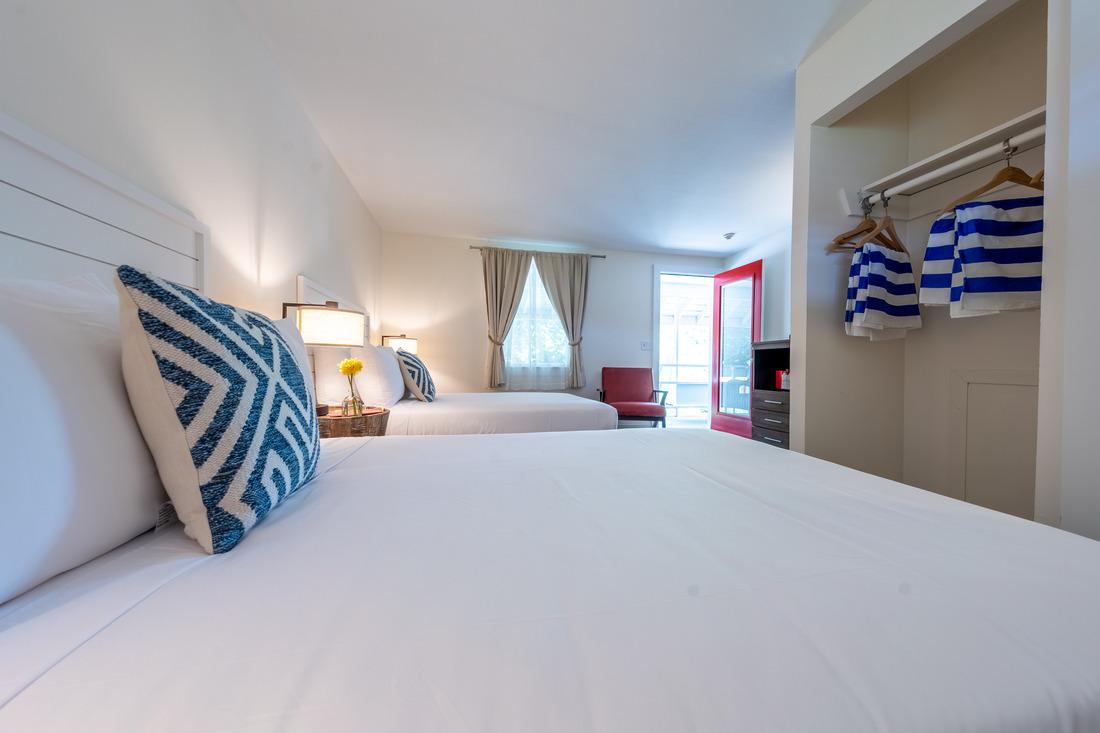 Two neatly made beds in a cozy bedroom with striped pillows and a red chair.