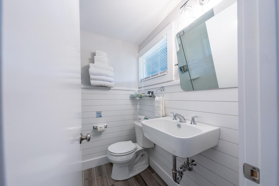 Small, bright bathroom with sink, toilet, and stacked towels.