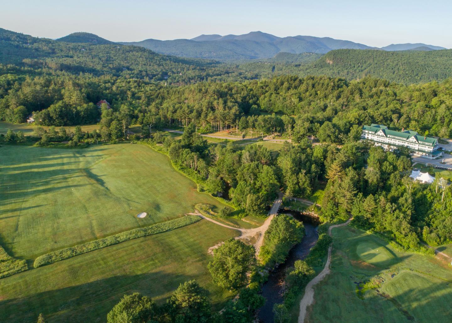 Aerial view of lush green fields and forested hills with mountains in the distance.