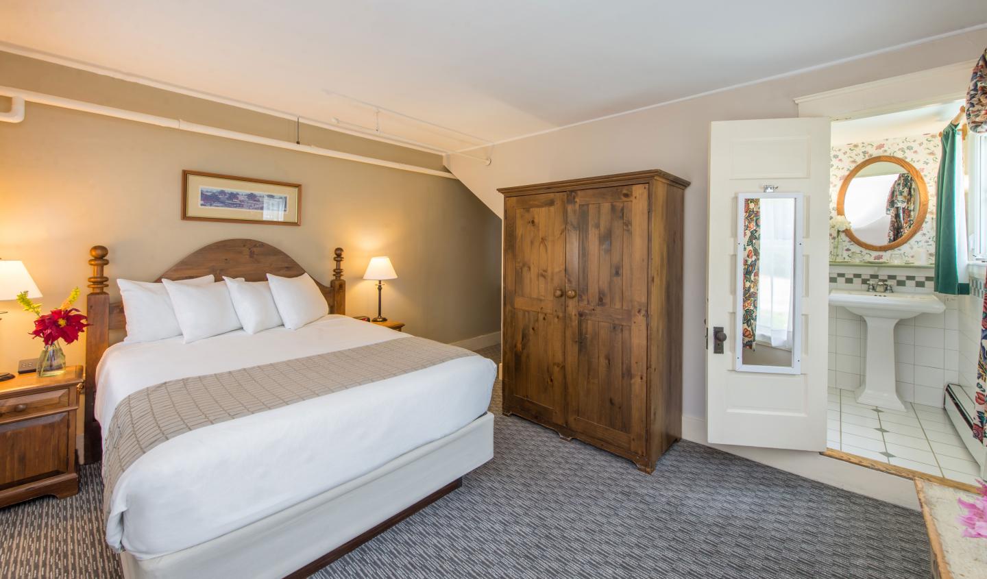 Cozy hotel room with a bed, wooden wardrobe, and a view into a bright bathroom.