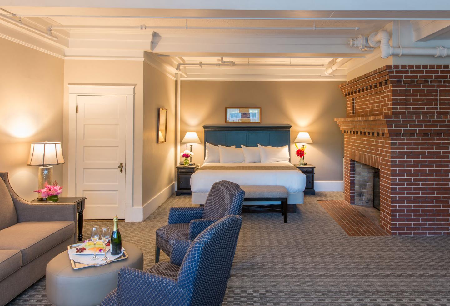 Cozy hotel room with bed, sofa, chairs, and brick fireplace.
