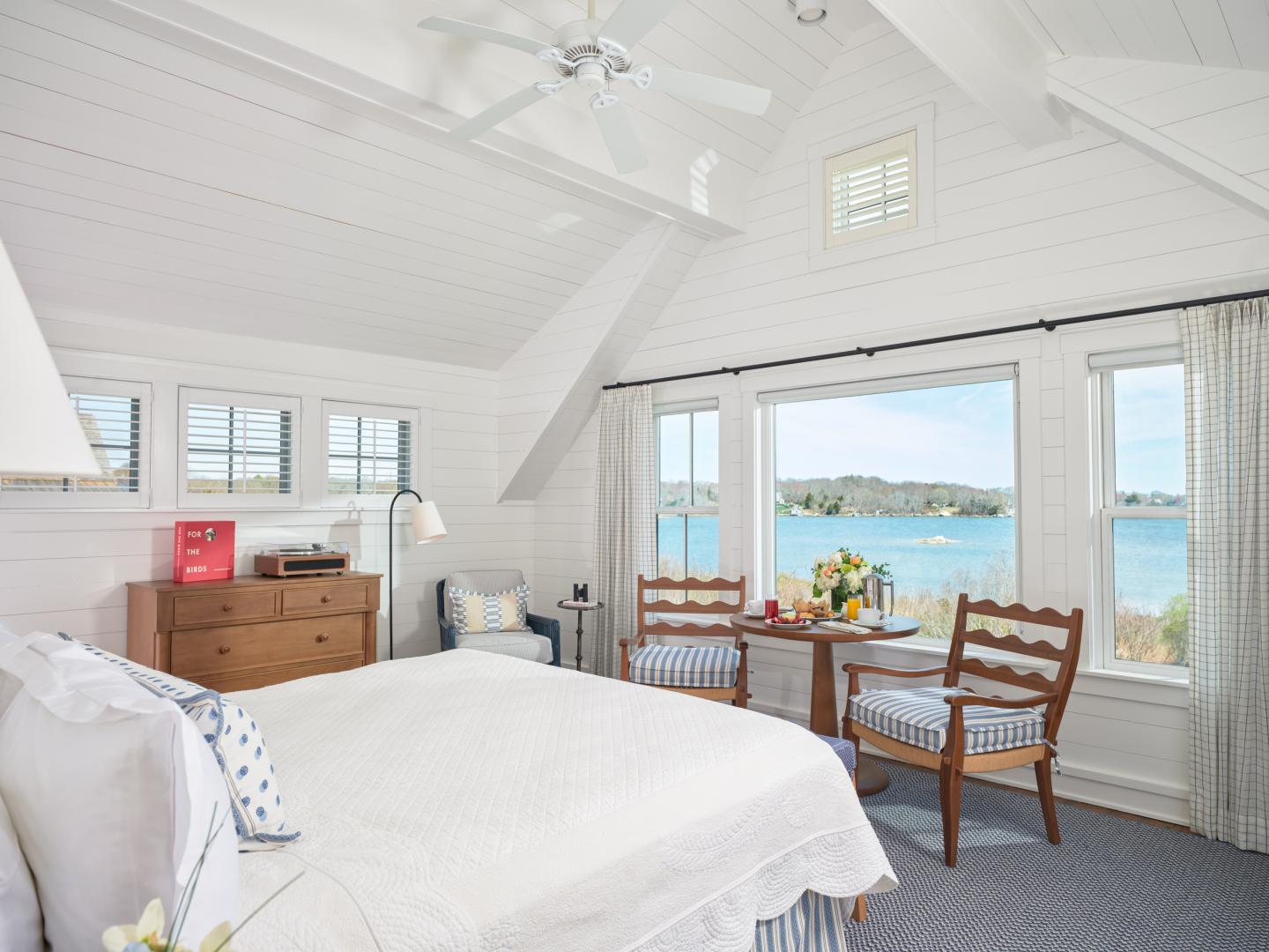 Cozy white bedroom with ocean view, wooden furniture, and soft lighting.