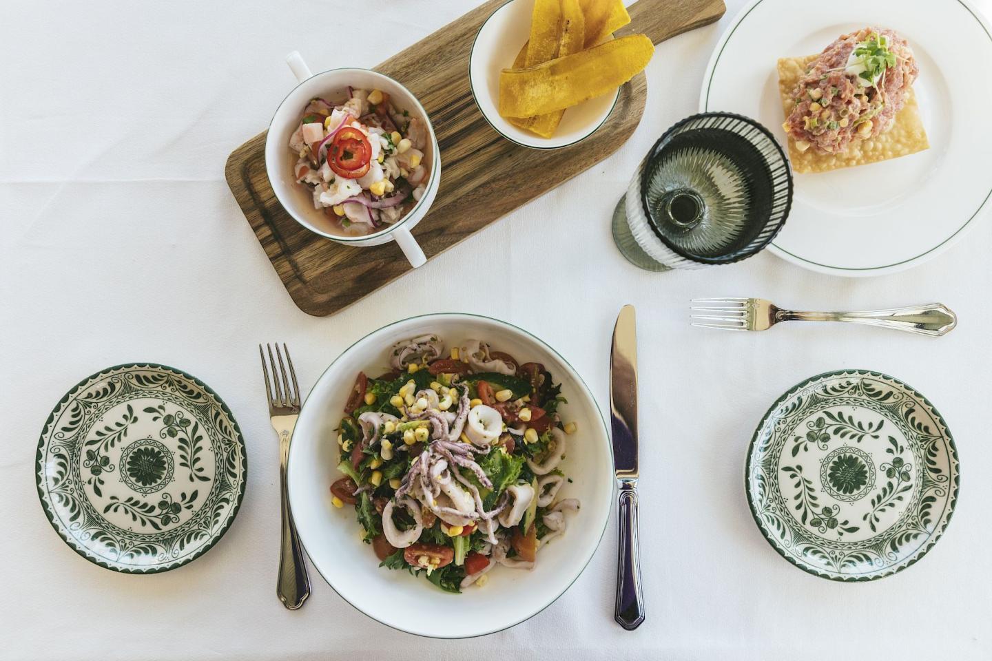 Elegant meal with ceviche, plantains, and salad on a white tablecloth.
