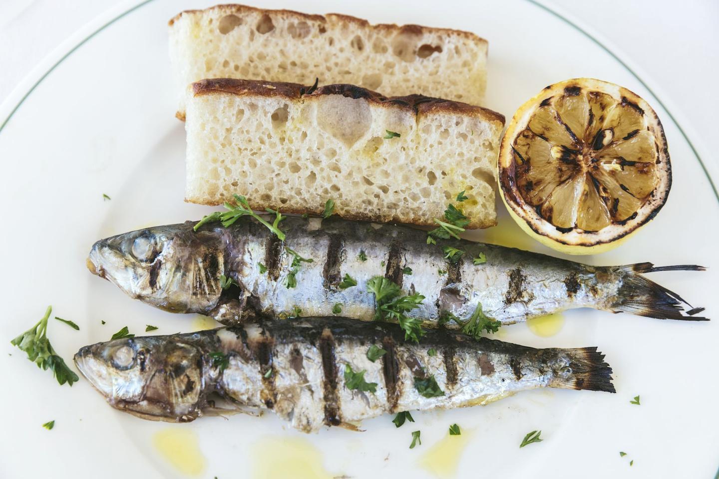 Grilled sardines with bread and lemon on a white plate.