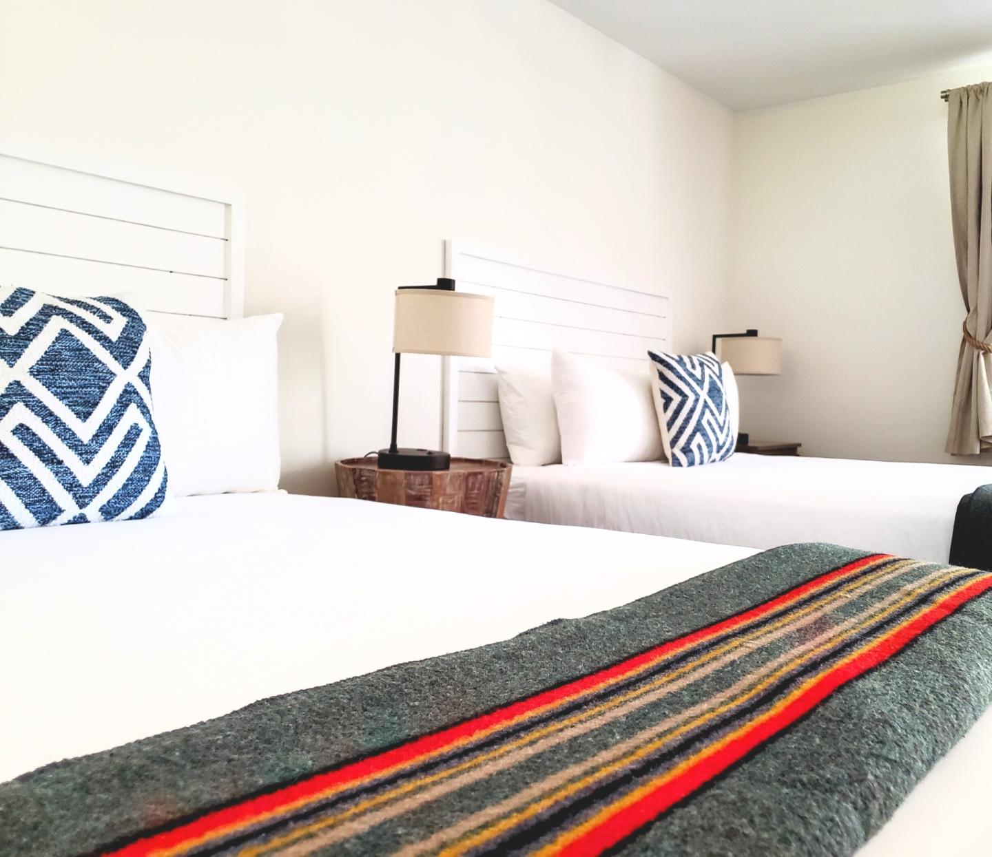 Two neatly made beds with patterned pillows in a bright room.