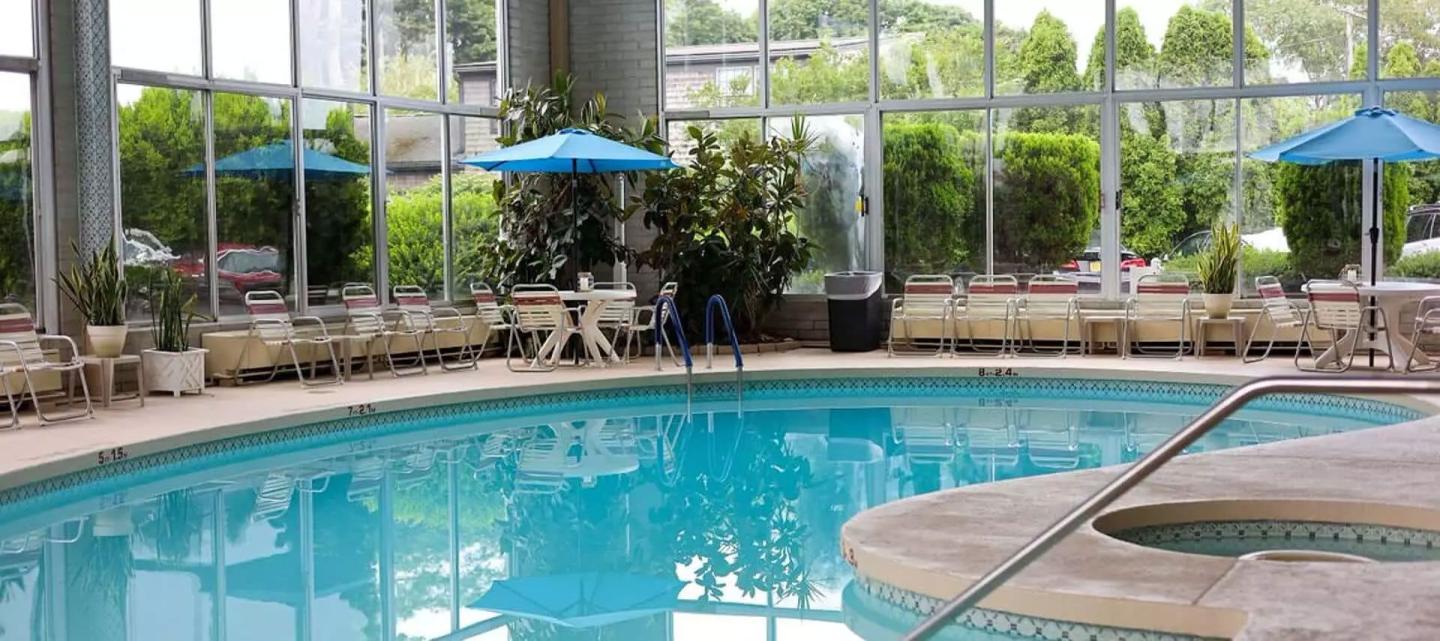 Indoor pool with blue umbrellas and greenery outside.