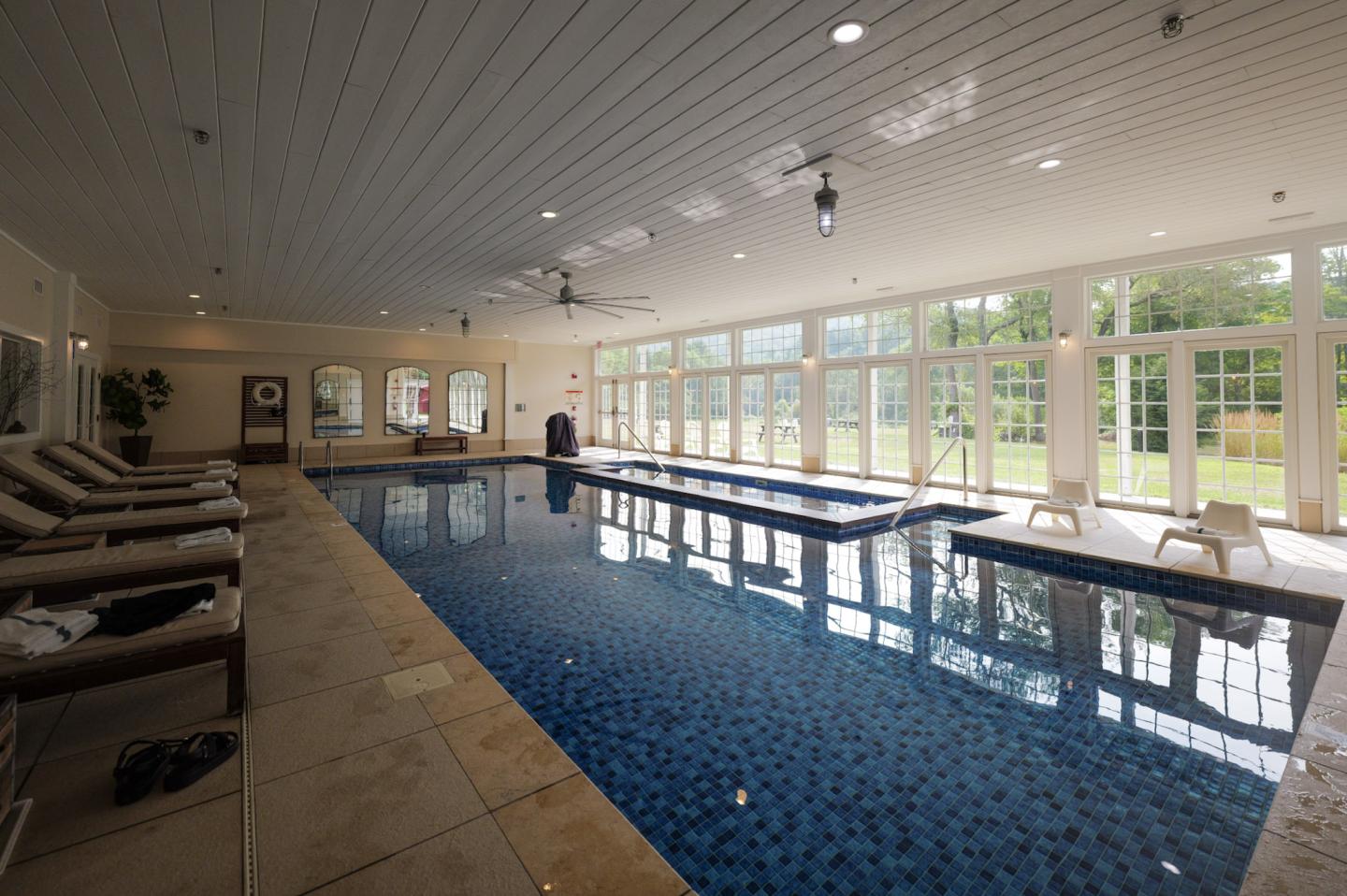 Indoor pool with lounge chairs and large windows.