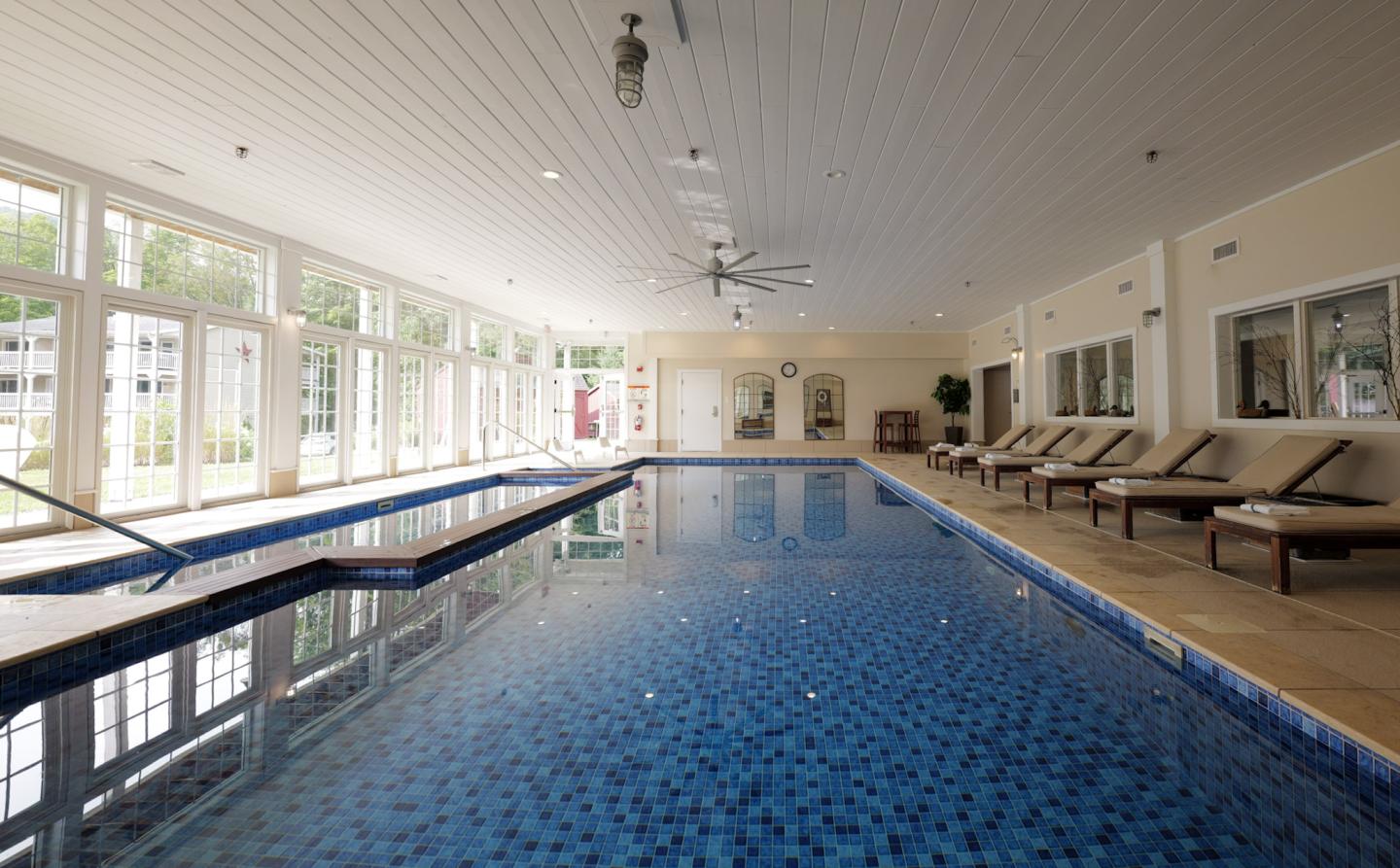 Indoor pool area with lounge chairs and large windows.